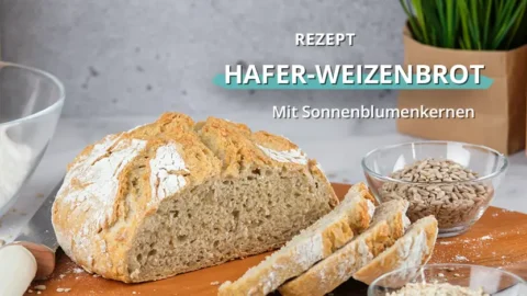 Aufgeschnittenes Weizenbrot auf einem Holzbrett neben einer Glasschale mit Körnern in einer Küchenumgebung