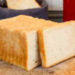 Frisch gebackenes Toastbrot auf einem Holzbrett in einer Küche vor einem roten Toaster