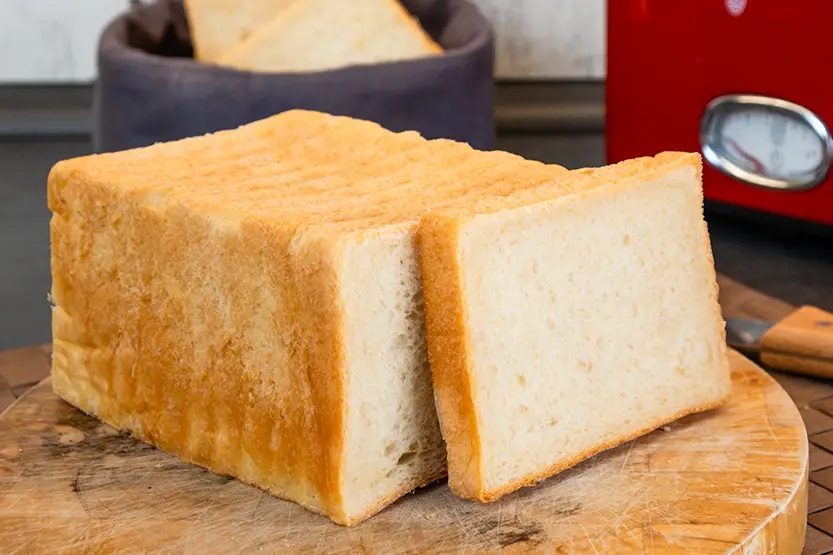 Frisch gebackenes Toastbrot auf einem Holzbrett in einer Küche vor einem roten Toaster