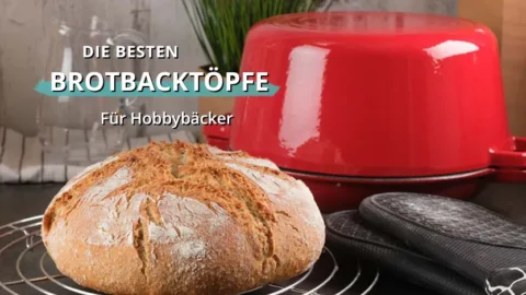 Rundes frisch gebackenes Brot auf einem Abkühlgitter vor einem roten gusseisernen Topf und Backhandschuhen