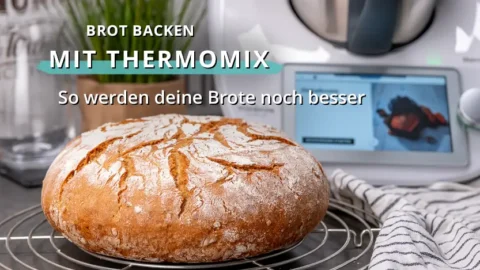 Frisch gebackenes rundes Brot auf einem Abkühlgitter vor einem Thermomix in einer Küchenumgebung