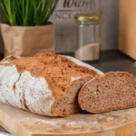 Aufgeschnittenes Emmer Vollkornbrot auf einem runden Holzbrett in einer Küchenumgebung